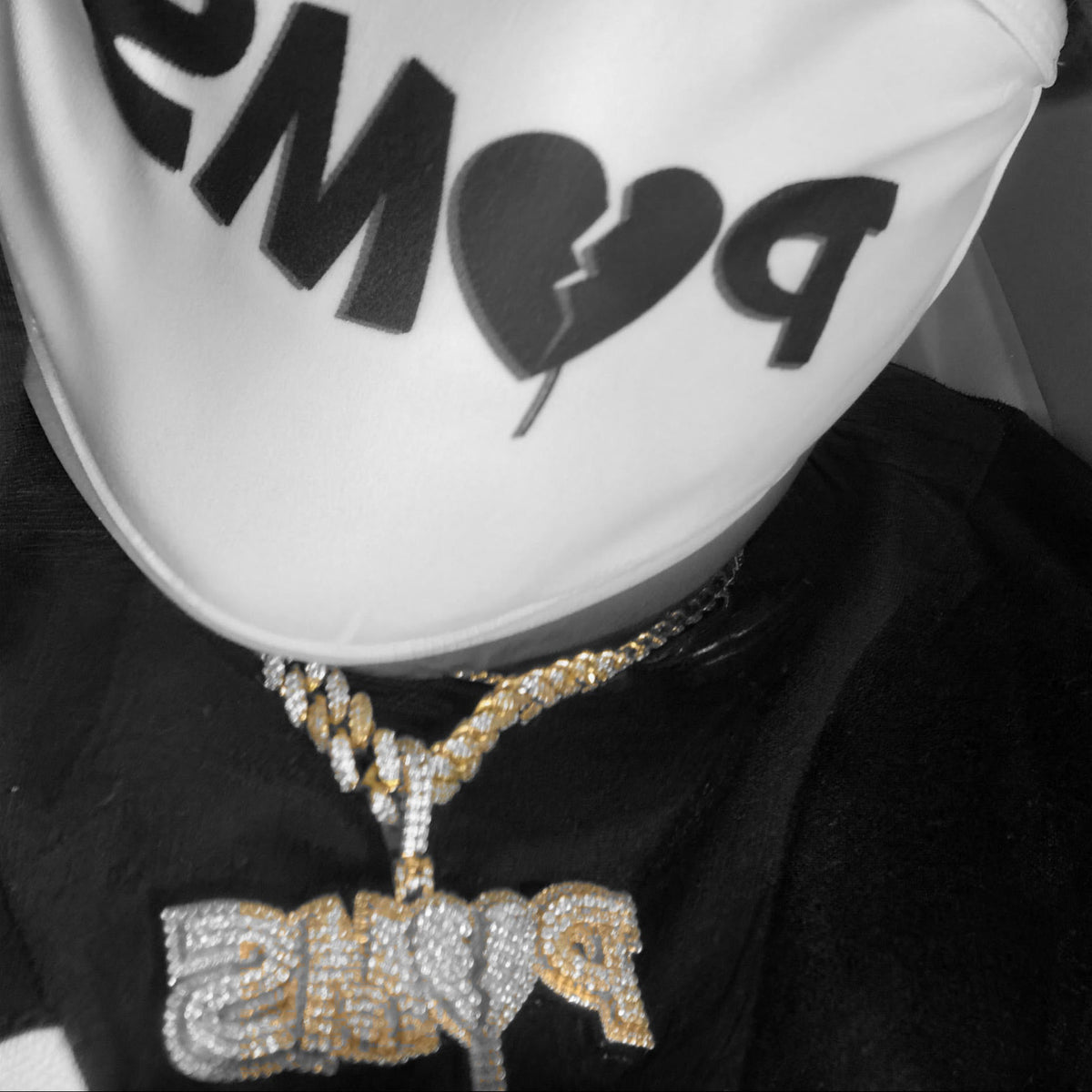 A close-up of a person wearing a white face mask with black 'PMS' lettering and a black knit beanie, along with layered gold and silver necklaces.