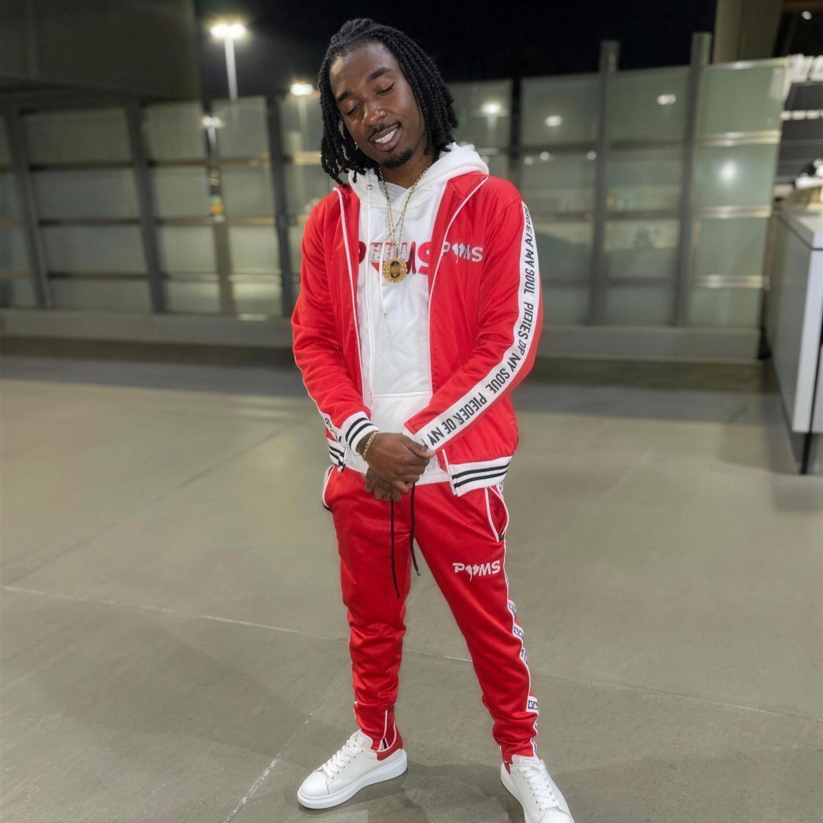 A man wearing a red and white POMS tracksuit with white sneakers, standing indoors