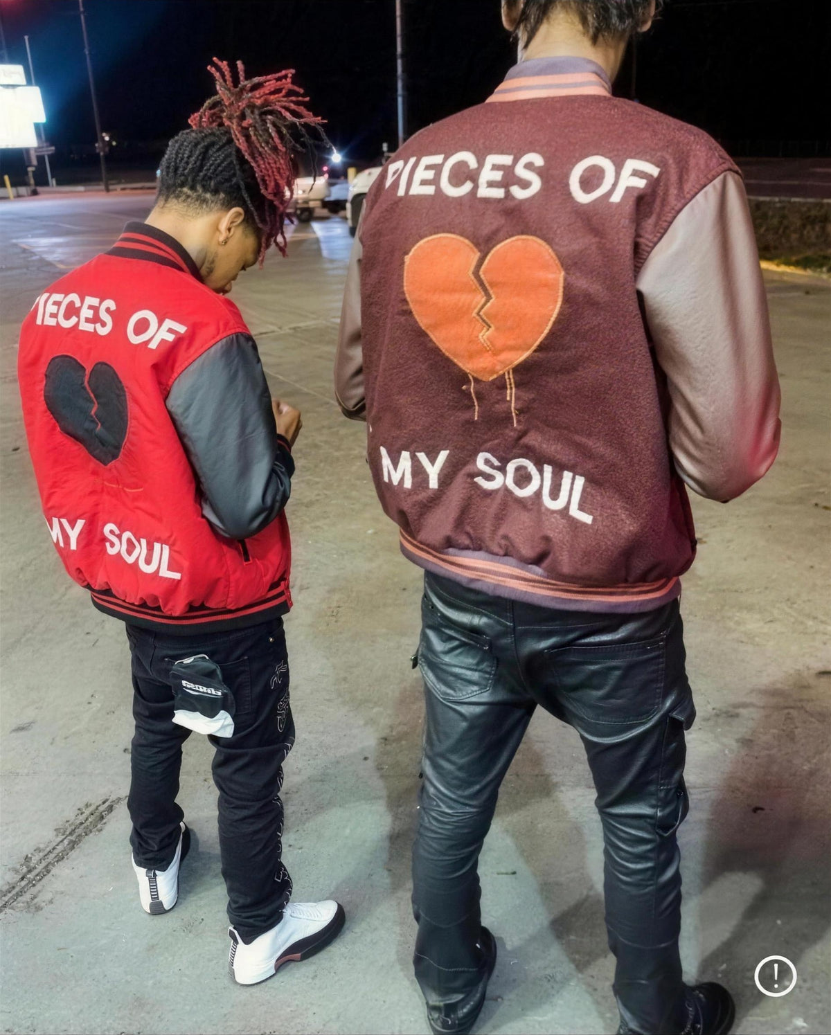 Two men wearing red and burgundy Pieces of My Soul varsity jackets with broken-heart graphics, seen from behind at night